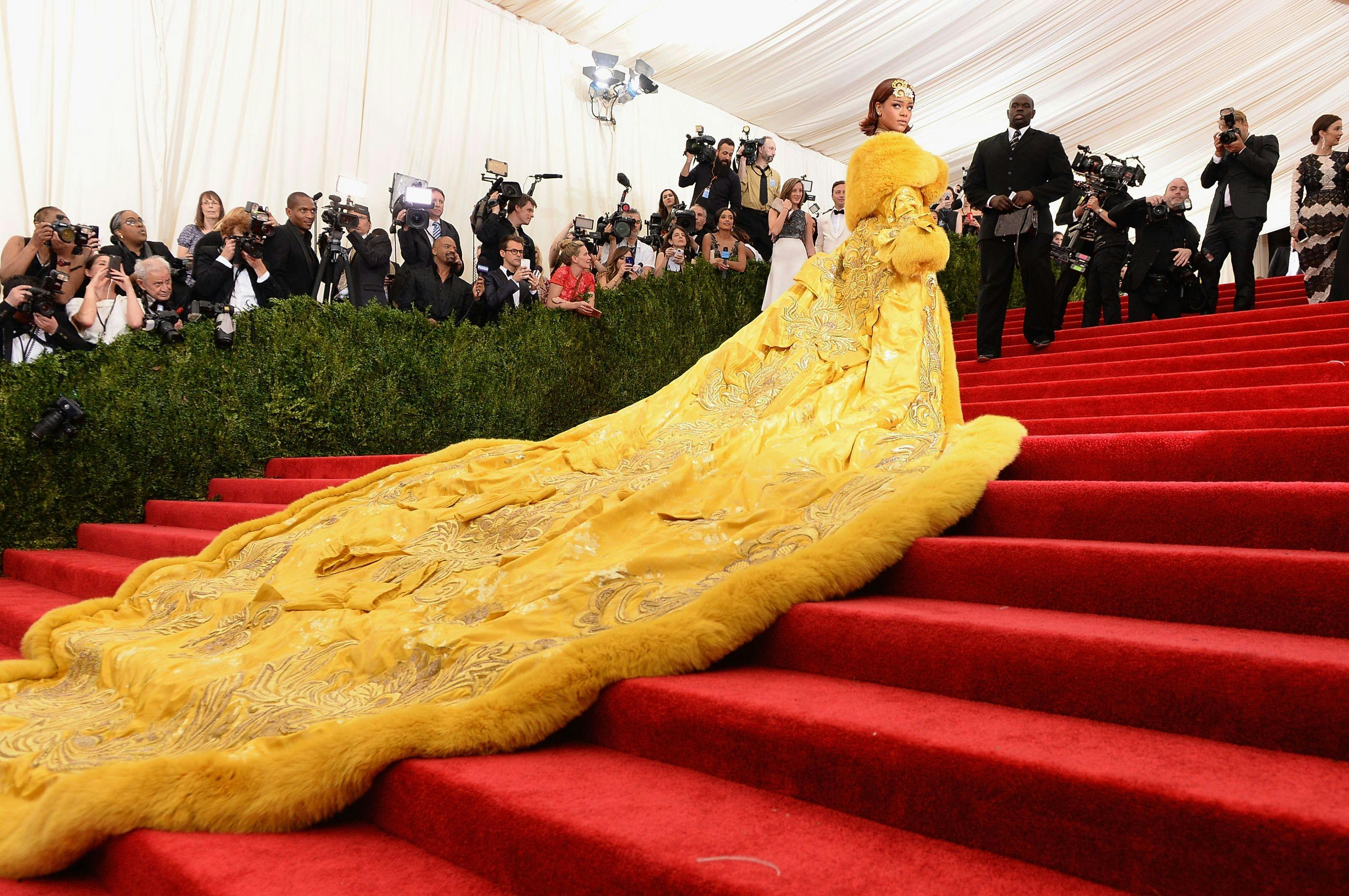rihanna in an elaborate yellow dress with a long train on the red met gala steps