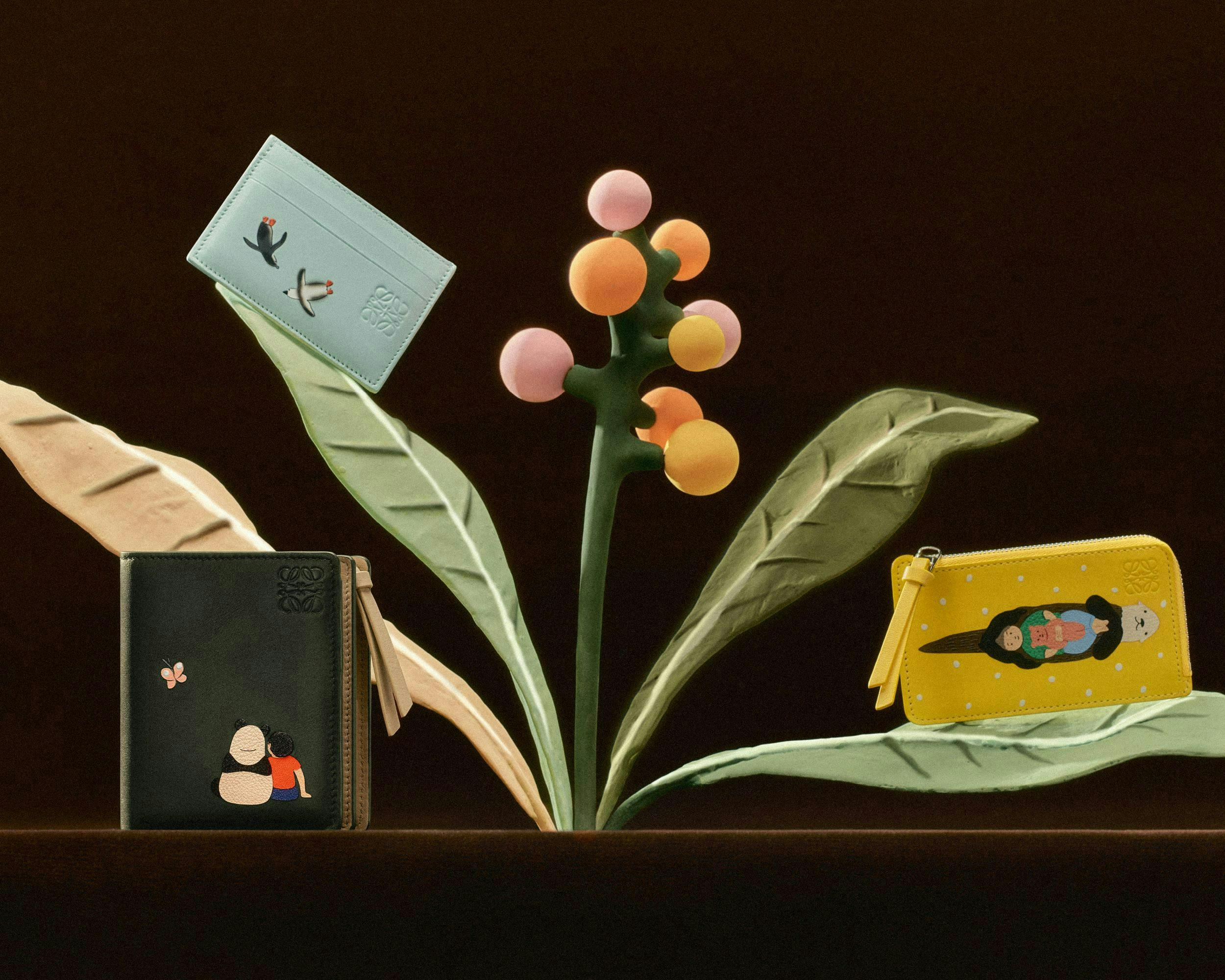 two wallets and a cardholder on a multicolored pastel plant for loewe's holiday campaign