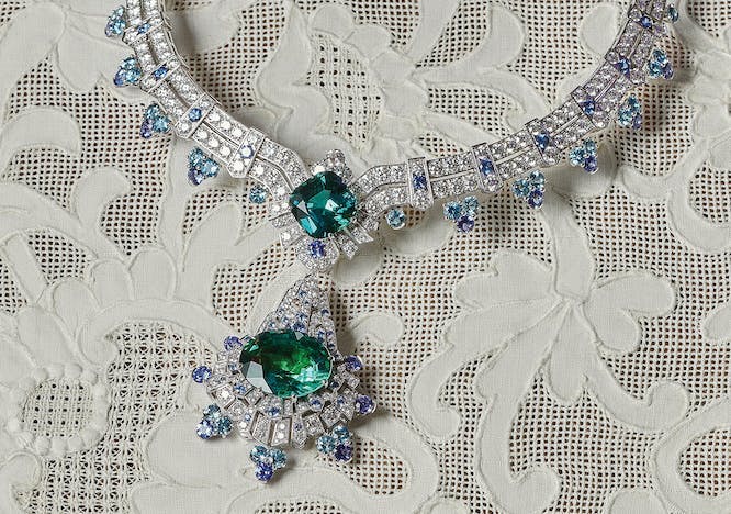 an emerald necklace with diamonds atop a lace cloth on a table