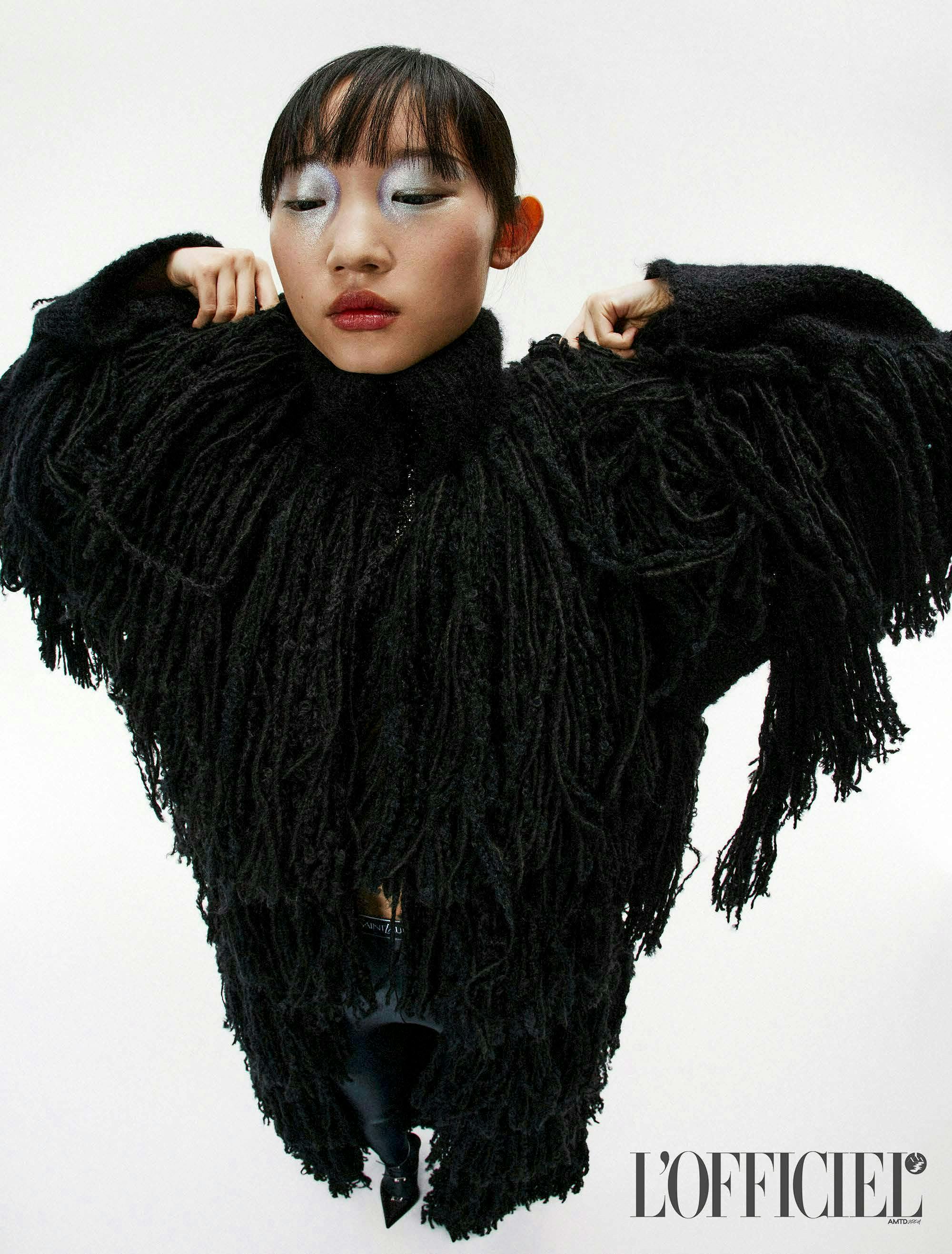 a model in a black fringe coat and wearing silver eyeshadow