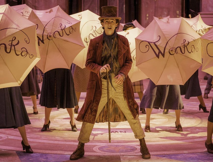 Timothée Chalamet standing in the middle of a crowd holding umbrellas that read "wonka"