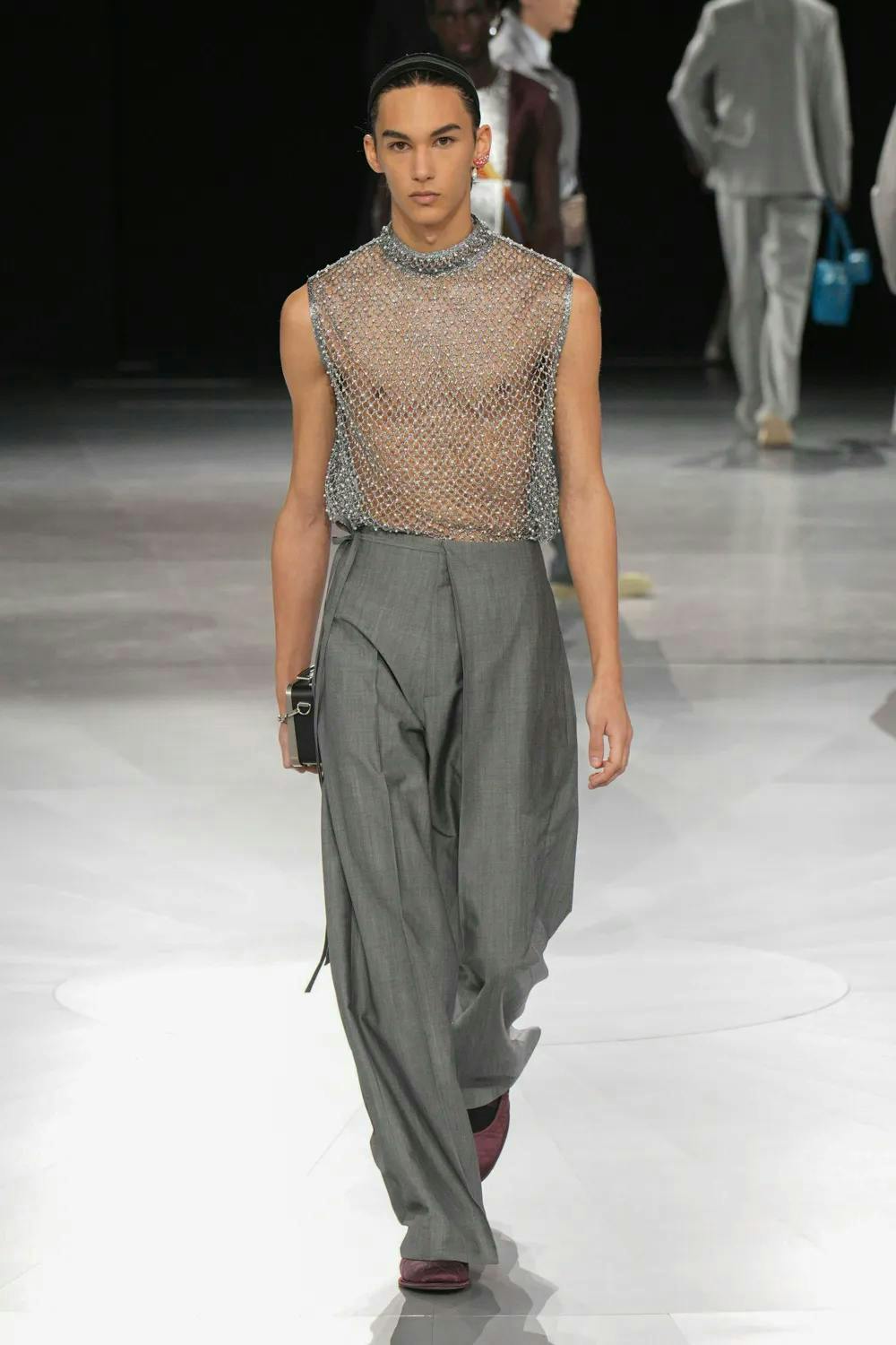 model on runway wearing mesh rhinestone top and gray pants