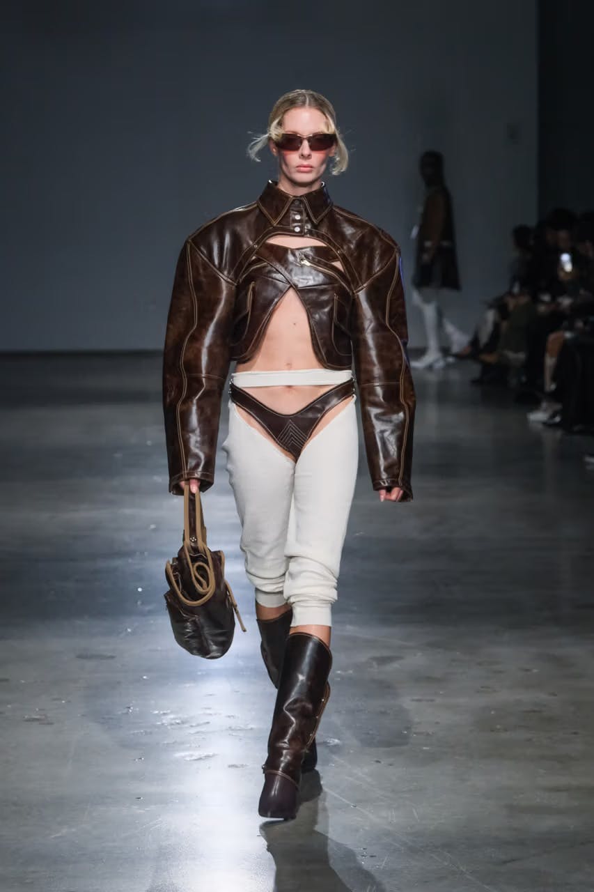 model on runway wearing brown coat with crisscross detail