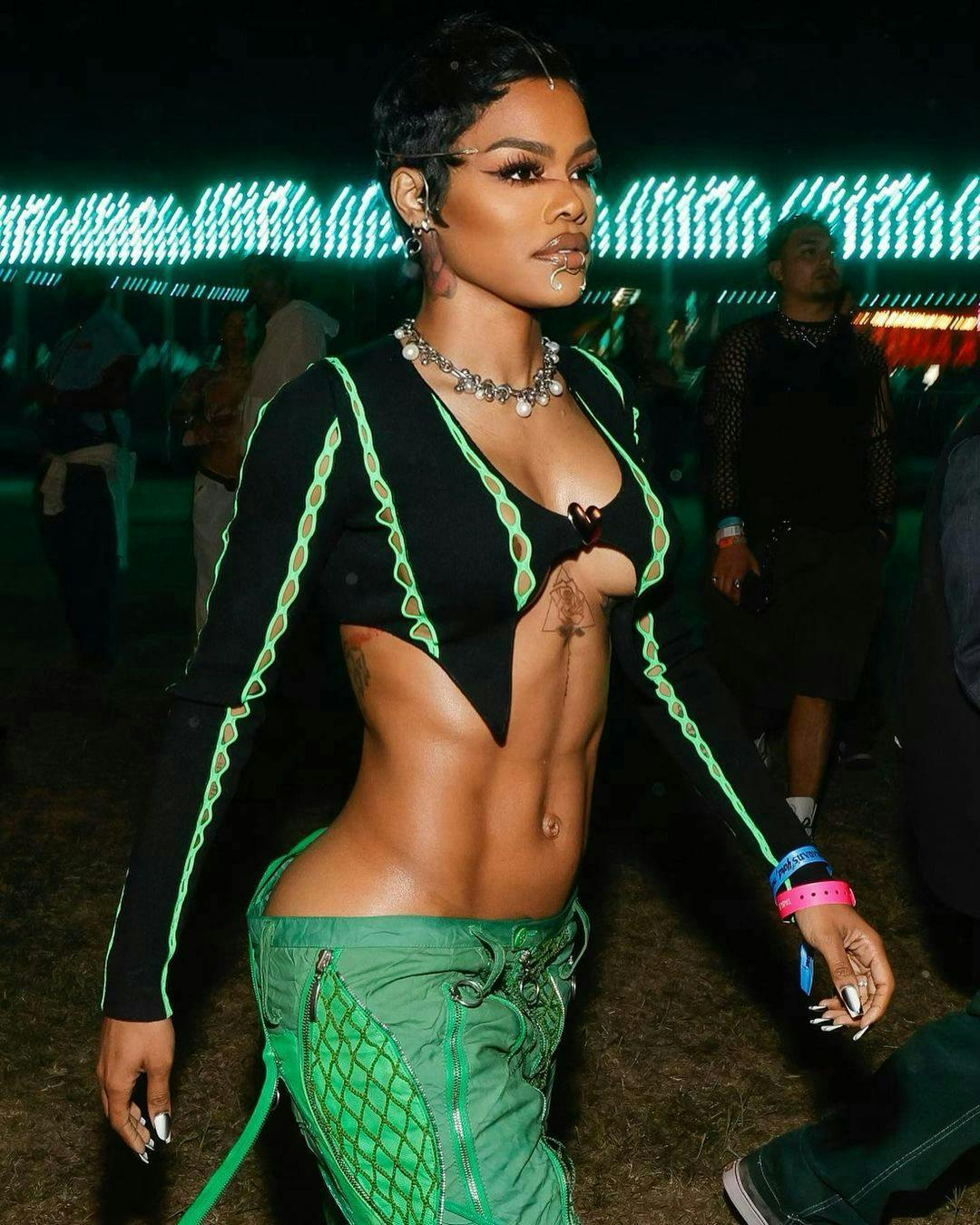 Teyana Taylor in green pants and a black long-sleeve bralette top with a graphic eye look at Coachella 2023.